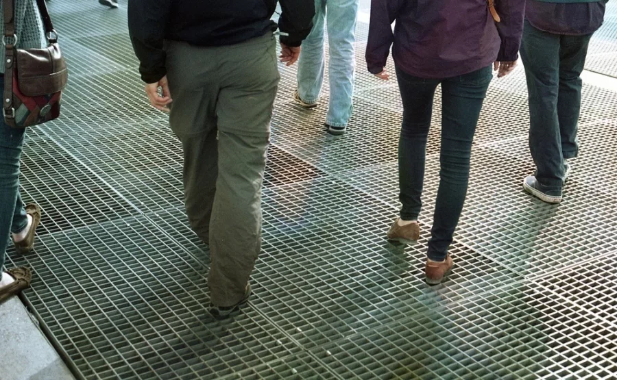 Five people, cropped from waist down, walking across a large grate.