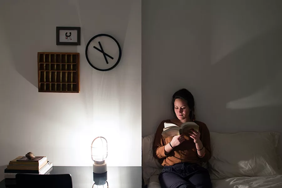 Timepeace clock on wall at night with girl reading book on bed beside it.